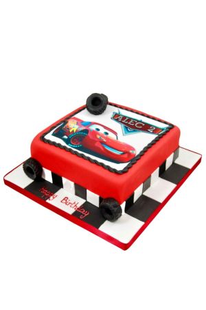 Vierkante rode verjaardagstaart van fondant met een eetbare afdruk van Bliksem McQueen, zwarte parelrand, 3D suiker autobanden op de hoeken en een finishvlag board gemaakt door The French Cake Company