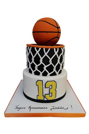 Gâteau d'anniversaire à deux étages sur le thème du basket avec base maillot blanc, étage central panier noir et filet blanc, surmonté d'un ballon 3D orange par The French Cake Company