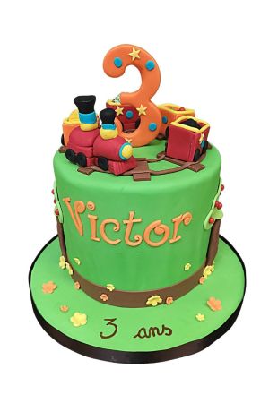 Gâteau d'anniversaire vert prairie avec circuit ferroviaire circulaire en bois, locomotive à vapeur rouge en relief et wagons remplis de charbon réalisé par The French Cake Company
