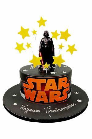Un gâteau d'anniversaire noir en pâte à sucre avec le logo Star Wars, une figurine de Dark Vador et des étoiles jaunes.
