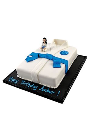Een rechthoekige verjaardagstaart in de vorm van een wit gevechtspak (kimono) met een blauwe band van fondant en een klein judo-poppetje.