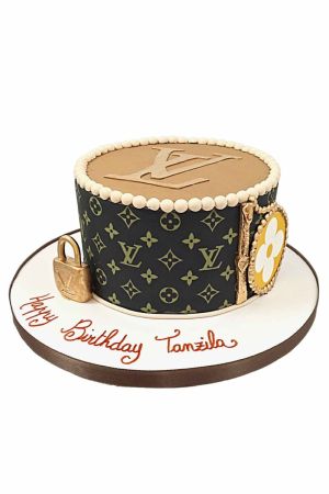 Un gâteau d'anniversaire de luxe décoré avec le motif monogramme Louis Vuitton, un cadenas doré en sucre et des charms de mode.