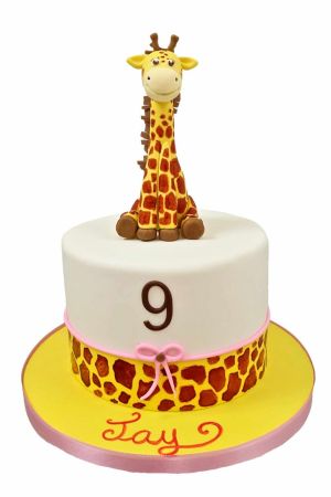Exclusieve witte verjaardagstaart met een giraf vlekkenrand, een roze strikje, het getal 9 en een ambachtelijk 3D zittend giraf figuurtje, van The French Cake Company.