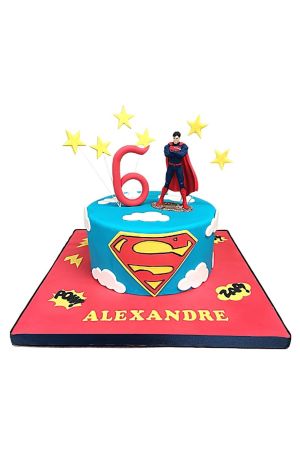Een blauwe fondant verjaardagstaart met het Superman logo, witte wolken, gele sterren en een 3D Superman figuurtje bovenop.
