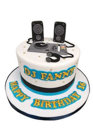 Un gâteau d'anniversaire blanc décoré d'un équipement de DJ en sucre modelé à la main, comprenant deux enceintes, une table de mixage, une platine et un casque audio.