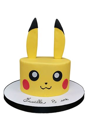 A round yellow fondant birthday cake decorated to look like Pikachu's face with big black eyes, red cheeks, a small smile, and two tall yellow and black ears standing up on top.