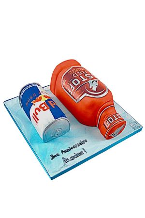Exclusieve 3D verjaardagstaart in de vorm van een Red Bull blikje en een oranje drankfles op een lichtblauw ijs-effect plateau, ontworpen door The French Cake Company.