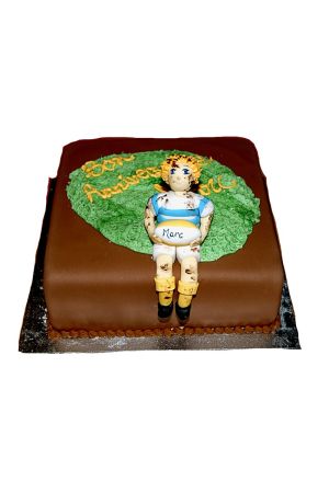 Un gâteau d'anniversaire carré marron décoré d'un terrain vert en pâte à sucre et surmonté d'une figurine modelée représentant un joueur de rugby tenant un ballon.