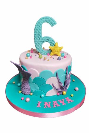 A pastel pink and turquoise birthday cake decorated with fondant mermaid scales, a purple mermaid tail, a yellow starfish, and a large turquoise number 6.