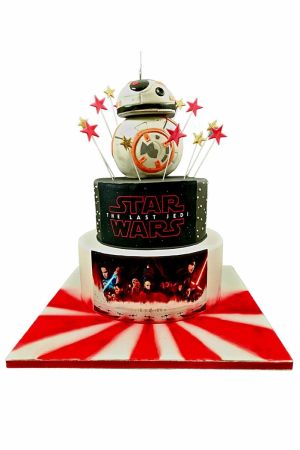A two-tier Star Wars The Last Jedi themed cake with a 3D BB-8 droid on top, surrounded by red and gold stars and edible movie scene photos.