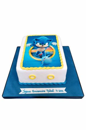Un gâteau d'anniversaire rectangulaire blanc avec une photo comestible de Sonic le Hérisson et des décorations en forme d'anneaux dorés.