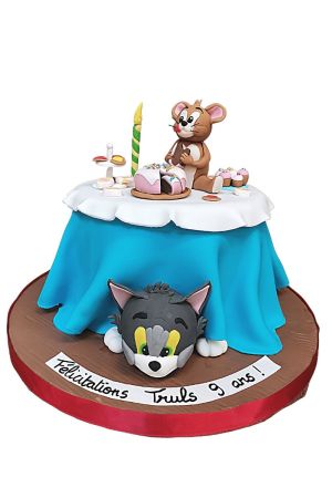 3D Tom and Jerry birthday cake styled like a table with Jerry mouse on top eating cake and Tom cat hiding underneath the blue tablecloth