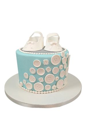 Gâteau de baptême bleu ciel à un étage, décoré de nombreux boutons blancs en sucre et surmonté d'une paire de chaussons blancs.