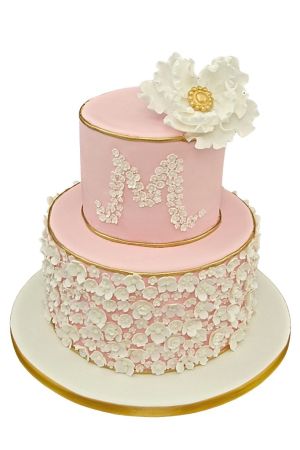 A luxurious two-tier pink communion cake covered in hundreds of small white sugar flowers with gold metallic edges and a large white flower on top.