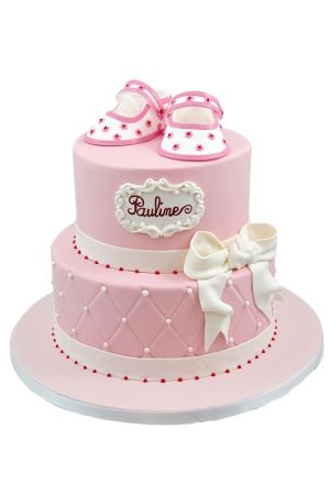 Gâteau de baptême rose à deux étages pour Pauline, décoré de chaussons de bébé comestibles, d'un nœud blanc et d'un glaçage matelassé.