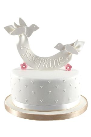 Gâteau de baptême blanc à un étage avec une bannière en sucre portée par deux colombes et de petites fleurs roses.
