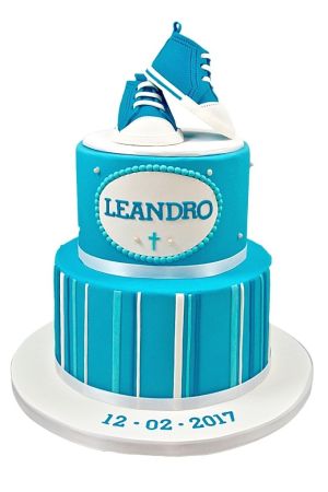 Gâteau de baptême bleu à deux étages avec des rayures blanches et des baskets de bébé en sucre au sommet.