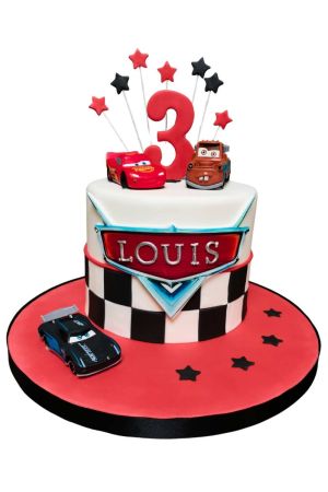 Round white birthday cake with checkered flag lower pattern, red cake board with black stars, toy figurines of Lightning McQueen, Tow Mater, Jackson Storm, and star toppers on wires by The French Cake Company