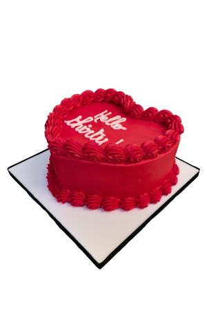 Un gâteau d'anniversaire rouge en forme de cœur, orné de bordures de crème cannelées volumineuses et d'un message personnalisé écrit en blanc au centre.