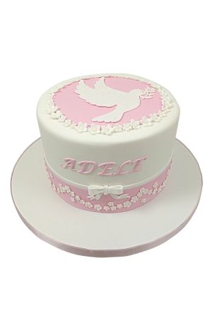 A single-tier white communion cake with a pink top and ribbon, featuring a white sugar dove and small white flowers.
