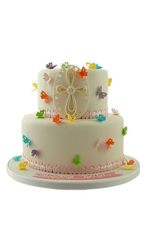 Un gâteau de communion blanc à deux étages orné de bordures en dentelle rose, d'une grande croix blanche et de nombreux papillons en sucre de toutes les couleurs.