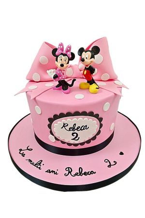 Een ronde roze fondant verjaardagstaart versierd met witte stippen, een grote roze suikerstrik met witte stippen en een naambordje voor de tweede verjaardag van Rebeca, bekroond met Mickey en Minnie Mouse poppetjes.