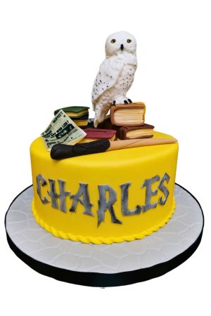 A round bright yellow fondant birthday cake decorated with large custom grey lettering, topped with a detailed 3D sugar model of Hedwig the snowy owl sitting on a stack of spellbooks next to a wand and a Daily Prophet newspaper.