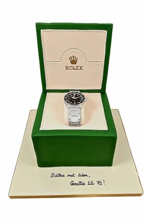 Un gâteau d'anniversaire conçu pour ressembler à une montre Rolex en argent, avec un message « Joyeux anniversaire » écrit sur le plateau du gâteau.