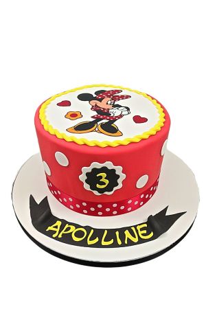 Un gâteau d'anniversaire rond rouge à pois blancs, surmonté d'une image comestible ronde de Minnie Mouse et d'un chiffre 3 à l'avant.