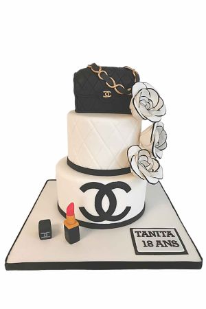Pièce montée d'anniversaire blanche surmontée d'un sac Chanel 3D noir matelassé avec chaîne dorée, fleurs de camélia blanches soulignées de noir, logo et rouge à lèvres en sucre réalisée par The French Cake Company