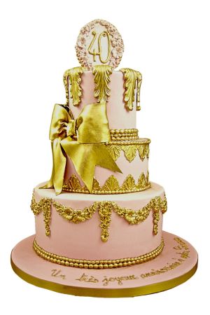 Une luxueuse pièce montée rose à trois étages décorée d'ornements en sucre dorés de style baroque et d'un grand nœud doré métallique.