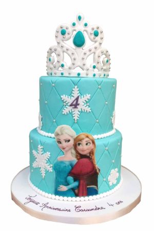 Gâteau d'anniversaire à deux étages bleu turquoise La Reine des Neiges matelassé avec perles de sucre, flocons blancs, chiffre 4 violet, visuel d'Elsa et Anna, couronné d'un diadème princier, créé par The French Cake Company.