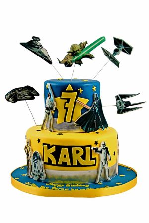 Un gâteau d'anniversaire à deux étages jaune et bleu sur le thème Star Wars avec des figurines de Yoda, Dark Vador et des vaisseaux spatiaux.