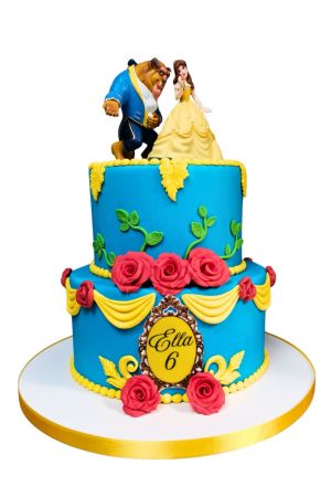 Grand two-tier ocean blue birthday cake with yellow fondant drapes, green leaf vines, handcrafted red roses, ornate gold frame, and Belle with Beast figures on top by The French Cake Company