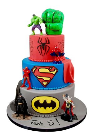 Gâteau d'anniversaire à trois étages décoré avec les logos et figurines de Batman, Superman, Thor, Spider-Man et un grand poing vert de Hulk.